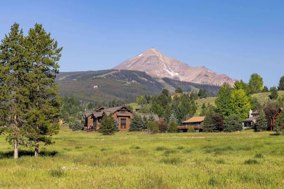 A mountain landscape with a prominent peak, surrounded by a grassy field and several wooden cabins.