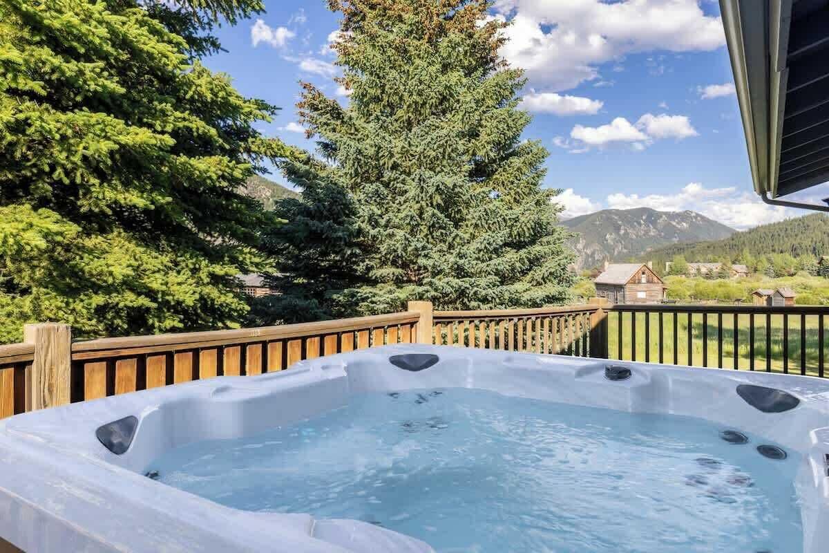 A hot tub on a deck with a view of a mountain and a house in the background.