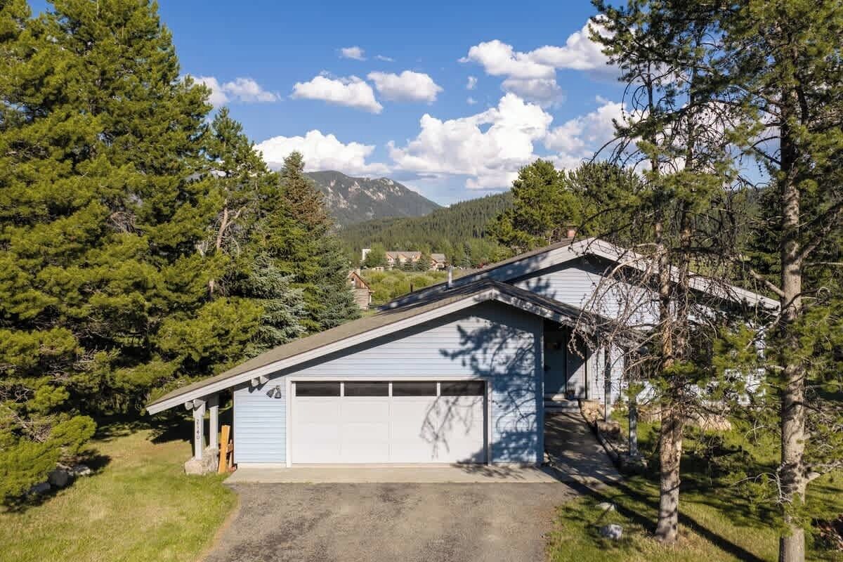 A single-story building with a garage, surrounded by trees and a mountain in the background.