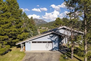 Ein eingeschossiges Gebäude mit Garage, umgeben von Bäumen und einem Berg im Hintergrund.