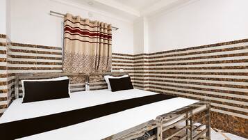 A hotel room with a bed, a bedside table, and a window with curtains.