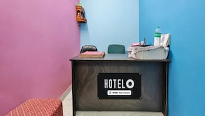 Un mostrador de recepción con un letrero que dice 'HOTELO OYO-Serviced' en una habitación con paredes de color rosa y azul.
