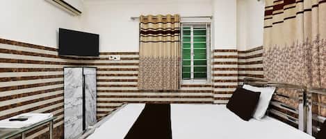 Una habitación de hotel con cama, televisión, ventana con cortinas y un mini bar.