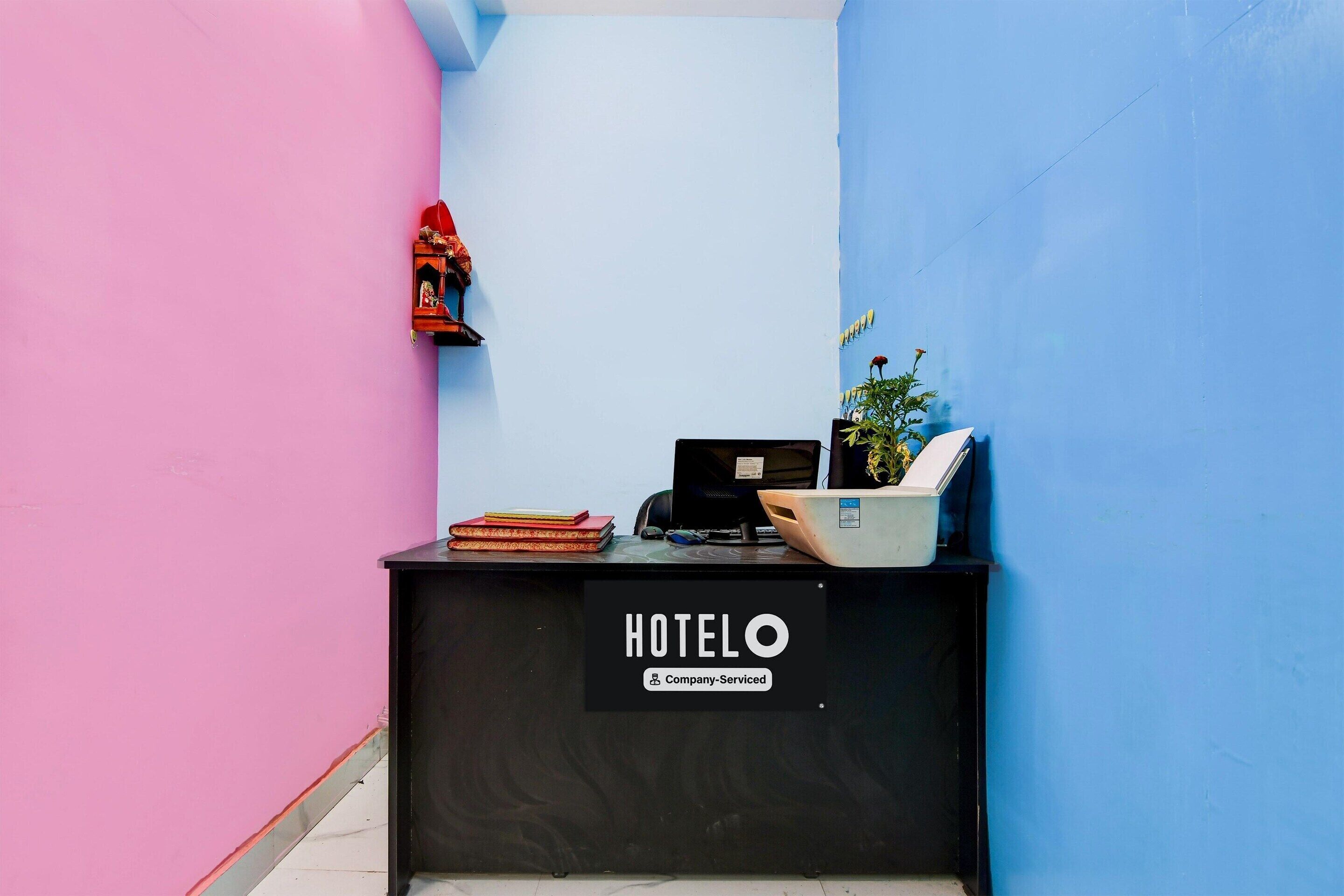 A reception desk with a sign reading 'HOTEL Company Serviced' in a room with pink and blue walls.