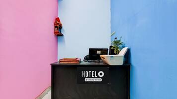 A reception desk with a sign reading 'HOTEL Company Serviced' in a room with pink and blue walls.