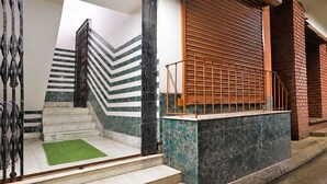 A staircase with a metal railing, a green carpet, and a brick wall. - Deluxe With Twin Bed Ayush Villa (Kolkata)