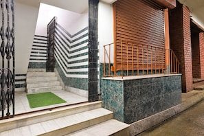 A staircase with a metal railing, a green carpet, and a brick wall. - Deluxe With Twin Bed Ayush Villa (Kolkata)