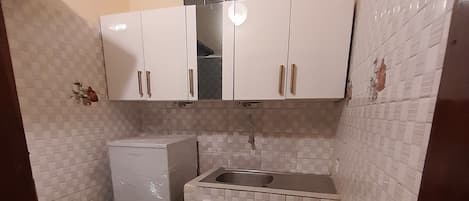A compact kitchen with white cabinets, a built-in sink, and a washing machine.