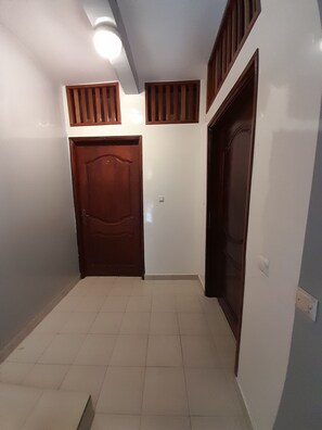 A hallway with two wooden doors, a tiled floor, and a ceiling light. - La Perle Noire: Furnished room or furnished two-bedroom apartment, 25 minutes from downtown Dakar. (GUEDIAWAYE)