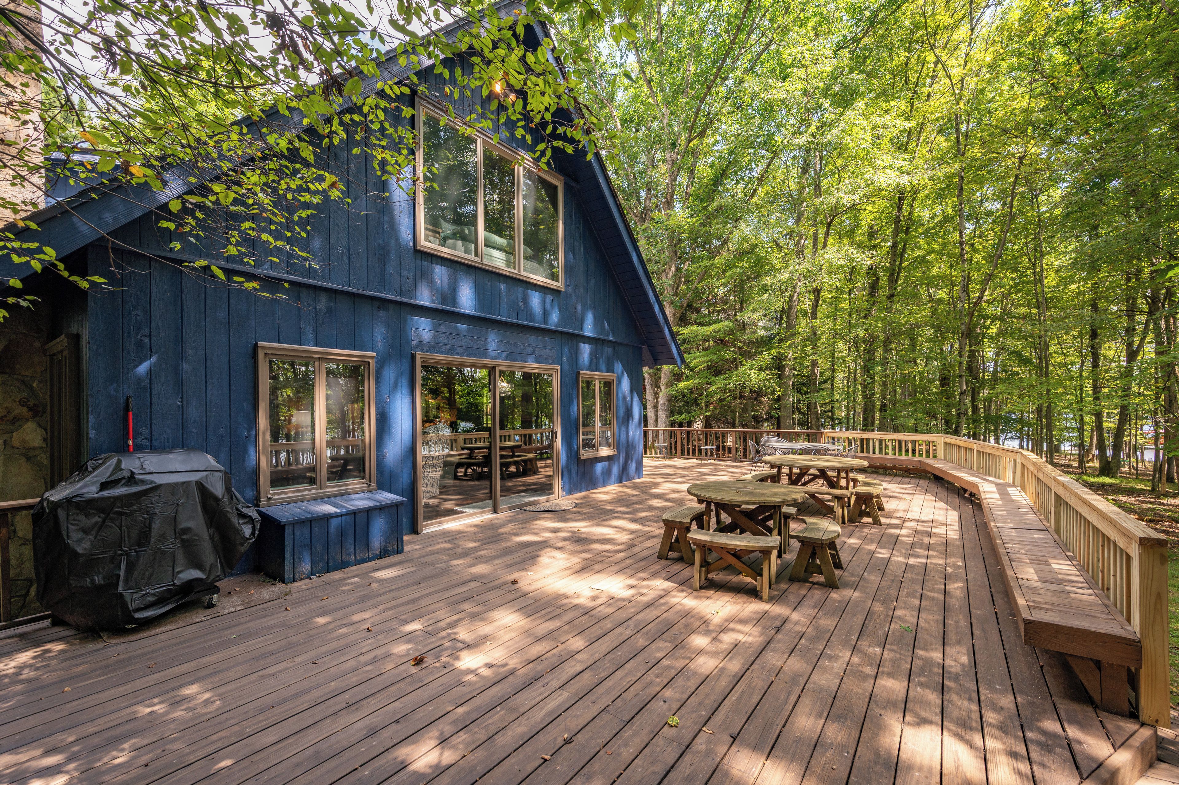 A blue wooden house with a deck, picnic tables, and a barbecue grill.