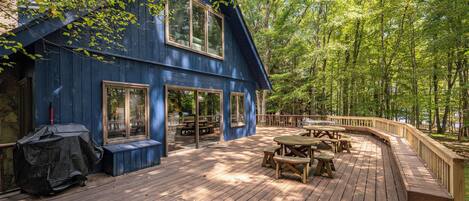 A blue wooden house with a deck, picnic tables, and a barbecue grill.