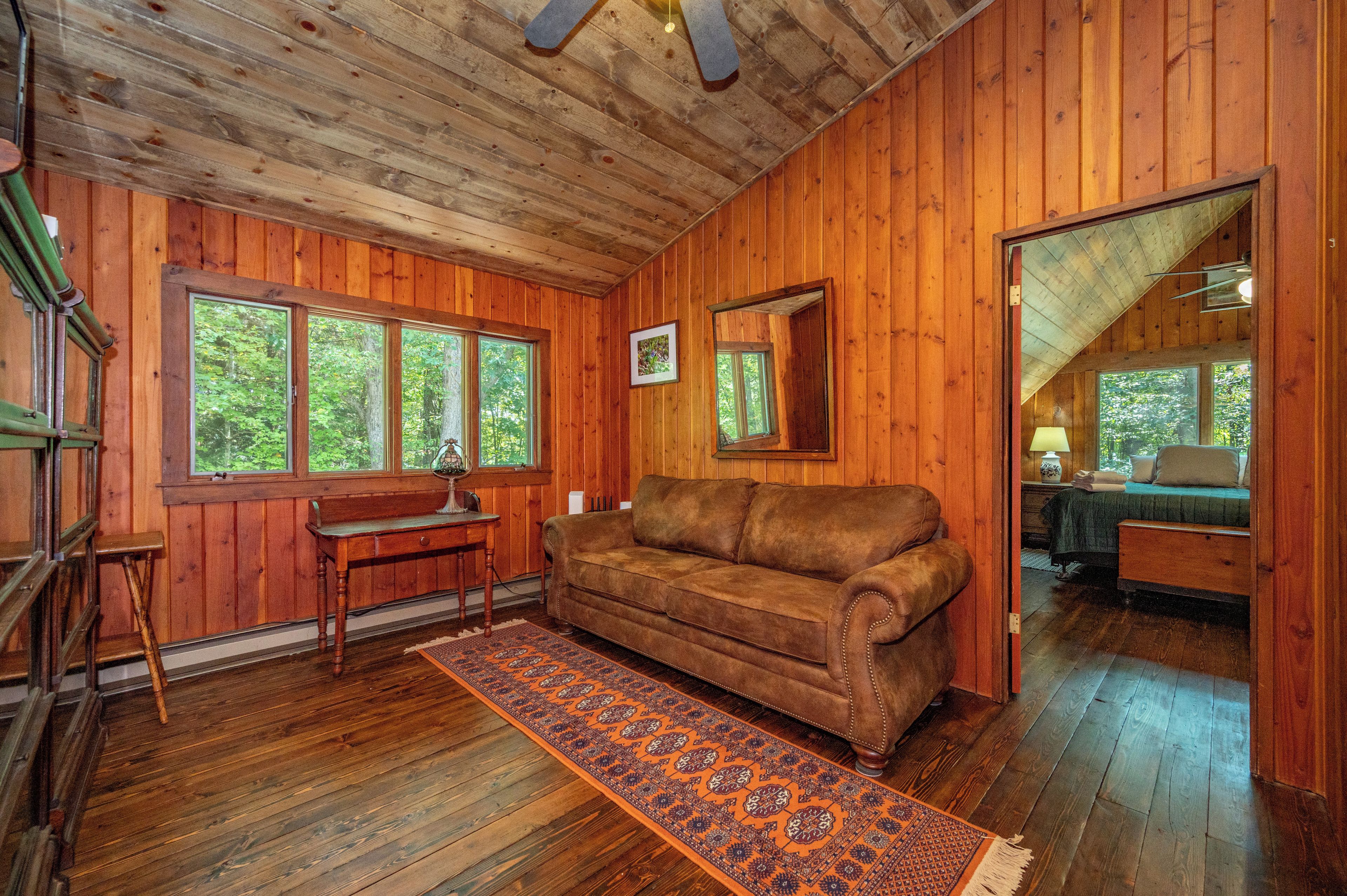 A wooden interior with a sofa, a desk, and a window overlooking greenery.