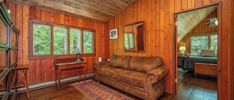 A wooden interior with a sofa, a desk, and a window overlooking greenery.