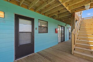 A building with a turquoise exterior, wooden deck, and a staircase leading to an upper level. - Poolside Condo with Beach Access (Gulf Shores)