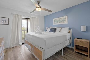 Ein Schlafzimmer mit Bett, Deckenventilator, Nachttisch und einem Fenster mit Vorhängen.