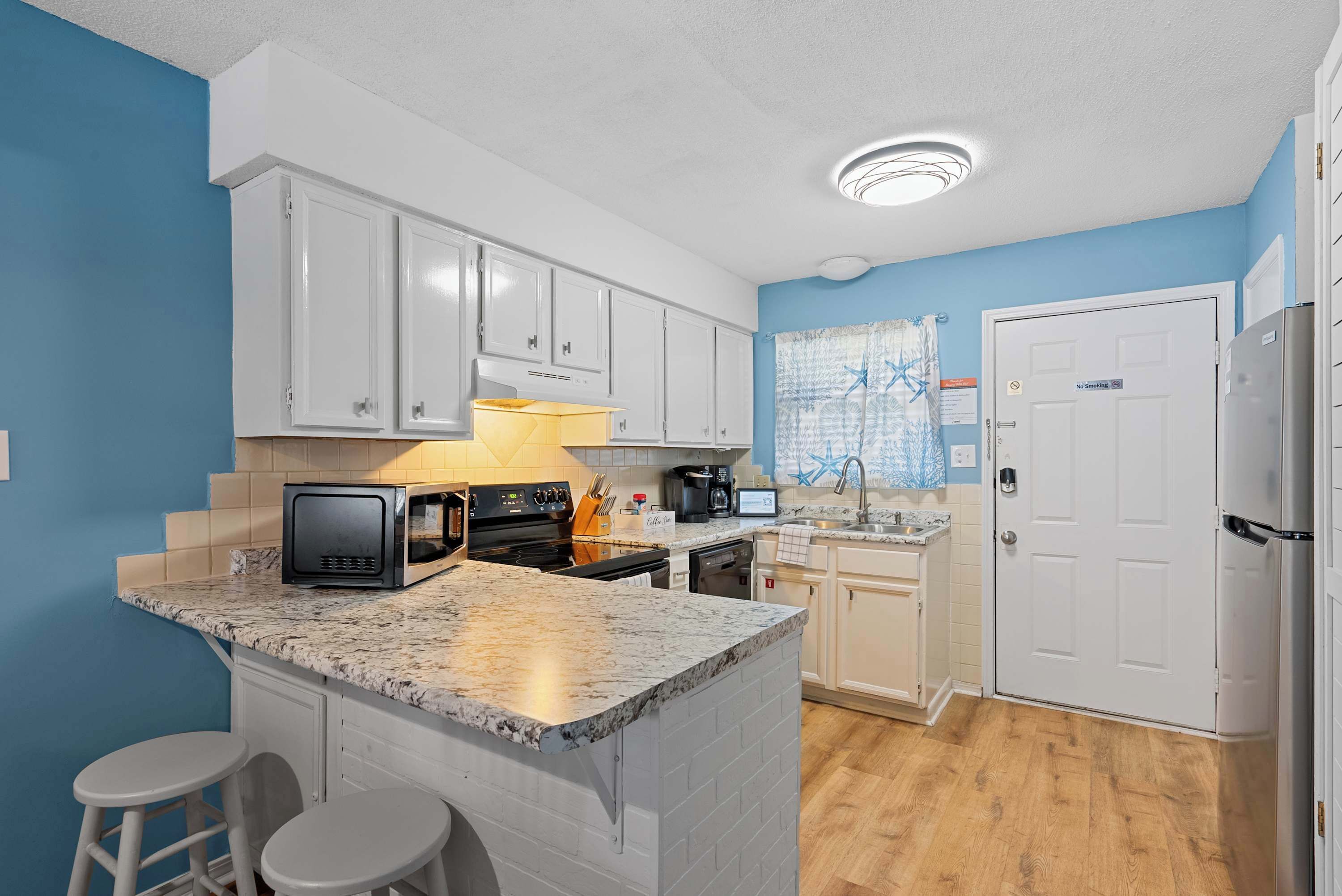 A kitchen with white cabinets, a granite countertop, a microwave, a stove, and a sink.