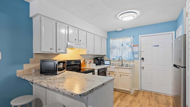 A kitchen with white cabinets, a granite countertop, a microwave, a stove, and a sink. - Poolside Condo with Beach Access (Gulf Shores)