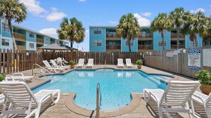 A swimming pool with lounge chairs, a wooden deck, and a wooden fence. - Poolside Condo with Beach Access (Gulf Shores)