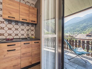 A kitchen with wooden cabinets and a tiled backsplash, leading to a balcony with a chair and a view of a mountainous landscape. - Apartment Ilda by Interhome (Morgex)