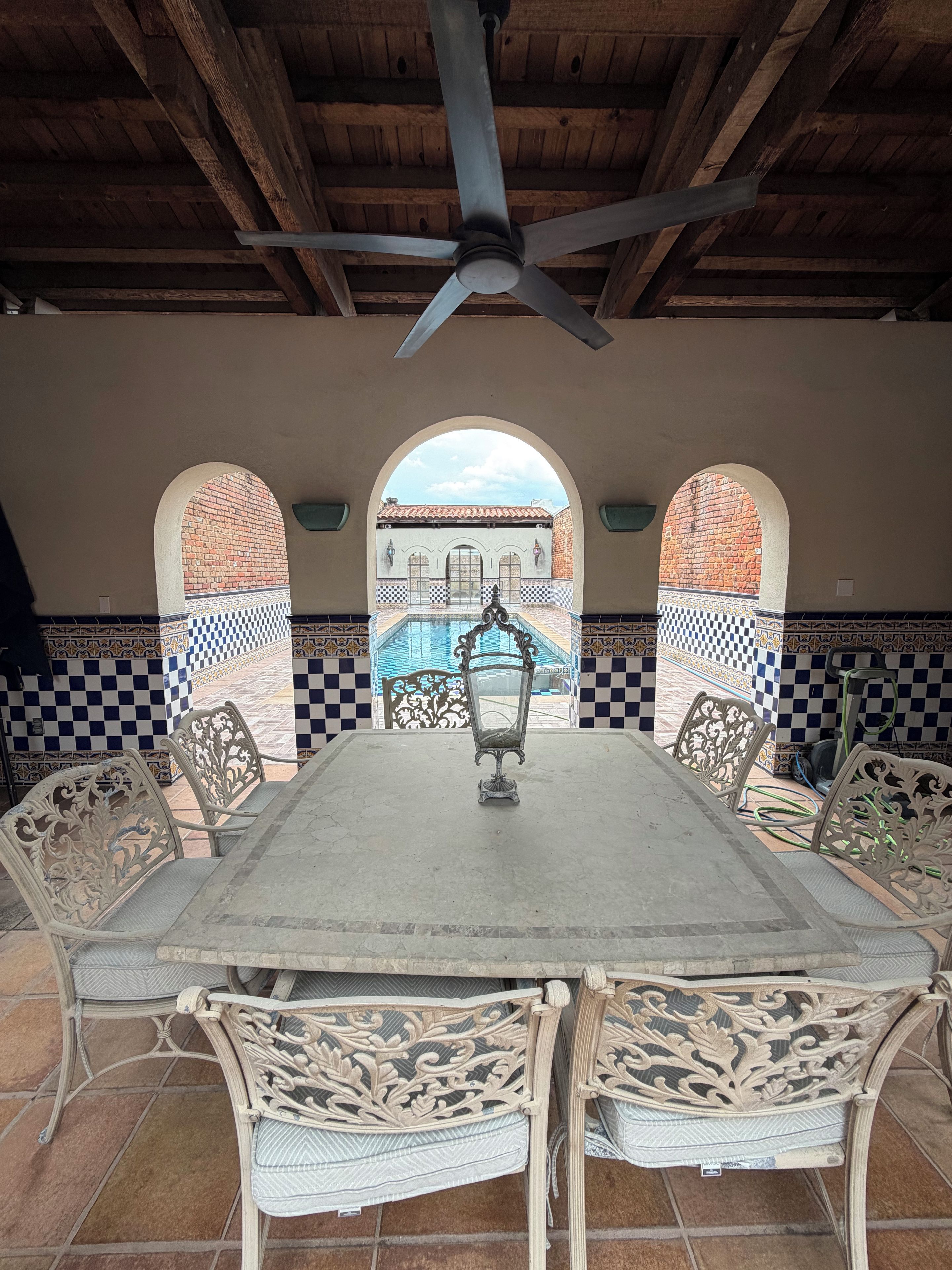 A covered patio with a table and chairs, a ceiling fan, and a view of a building with arches.