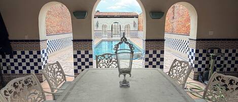A covered patio with a table and chairs, a ceiling fan, and a view of a building with arches.