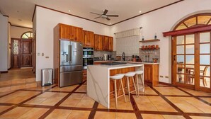 A spacious kitchen with wooden cabinets, a stainless steel refrigerator, and a large island with bar stools. - 3BR Retreat | Infinity Pool | Sunsets (Las Catalinas)