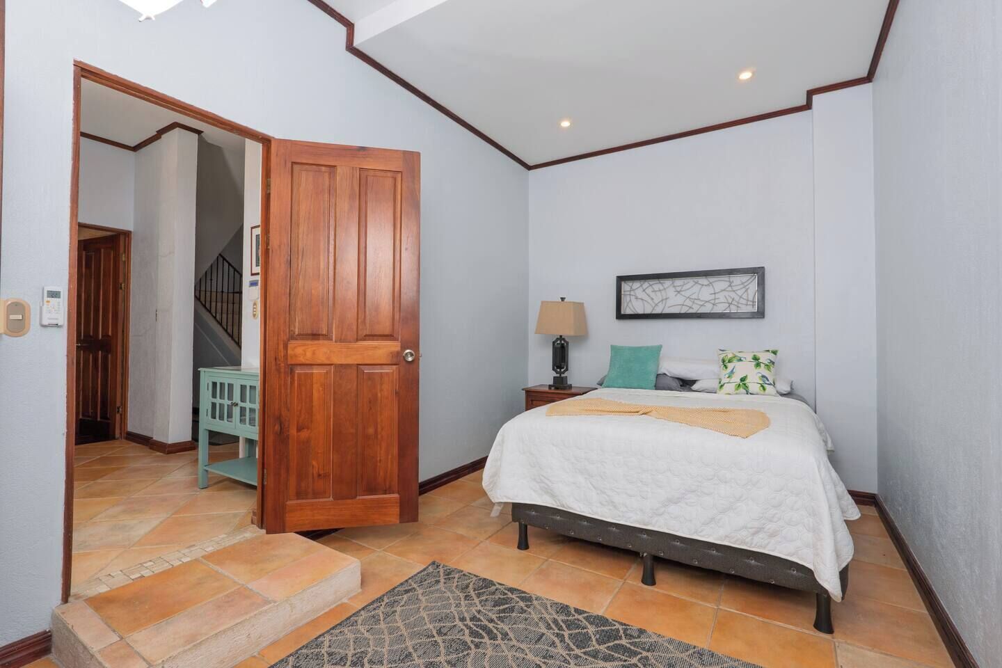 A bedroom with a bed, bedside table, lamp, and a door leading to a staircase.