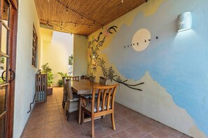 Zona pranzo con tavolo e sedie in legno, un murale decorativo e un soffitto con motivo bamboo.