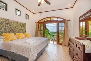 Ein Schlafzimmer mit einem Bett, einem Schminktisch, einem Deckenventilator und Blick durch eine offene Tür.