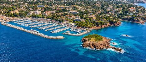 An aerial view of a marina with numerous boats docked, surrounded by residential buildings and a rocky coastline.
