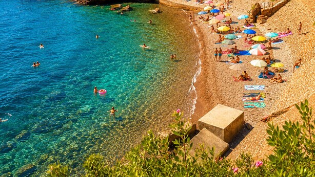 A beach with clear water, people swimming and sunbathing, and a rocky cliff in the background. - Apartment Le Mistral by Sur la mer (Saint Raphael)