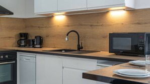A modern kitchen with a wooden backsplash, a black faucet, a coffee maker, a microwave, and white cabinets. - Apartment Le Mistral by Sur la mer (Saint Raphael)