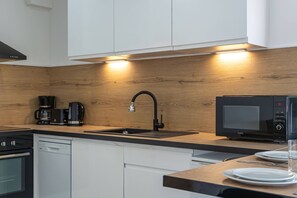 Eine moderne Küche mit Holzrückwand, einem schwarzen Wasserhahn, einer Kaffeemaschine, einer Mikrowelle und weißen Schränken.