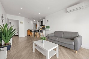 Ein modernes Wohnzimmer mit einem grauen Sofa, einem weißen Couchtisch und einer Küche im Hintergrund.