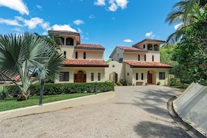 A two-story building with a tiled roof, a central entrance with a wooden door, and a paved driveway leading to the entrance. - 3 BR Home | Ocean Views, Sunsets, Pool in Paradise (Las Catalinas)