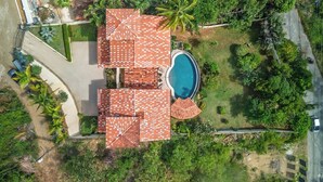 A residential property with a swimming pool, multiple roofed areas, and surrounding greenery.