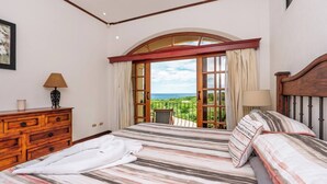 Ein Schlafzimmer mit einem großen Bett, einer Holzkommode und einem Balkon mit Meerblick.