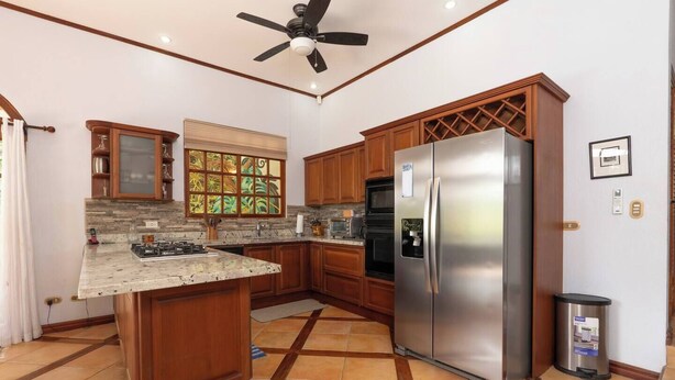 A kitchen with wooden cabinets, a stainless steel refrigerator, a gas stove, and a window with a view of greenery.