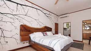 A bedroom with a wooden bed, a wall mural, a bathroom with a mirror, and a ceiling fan.
