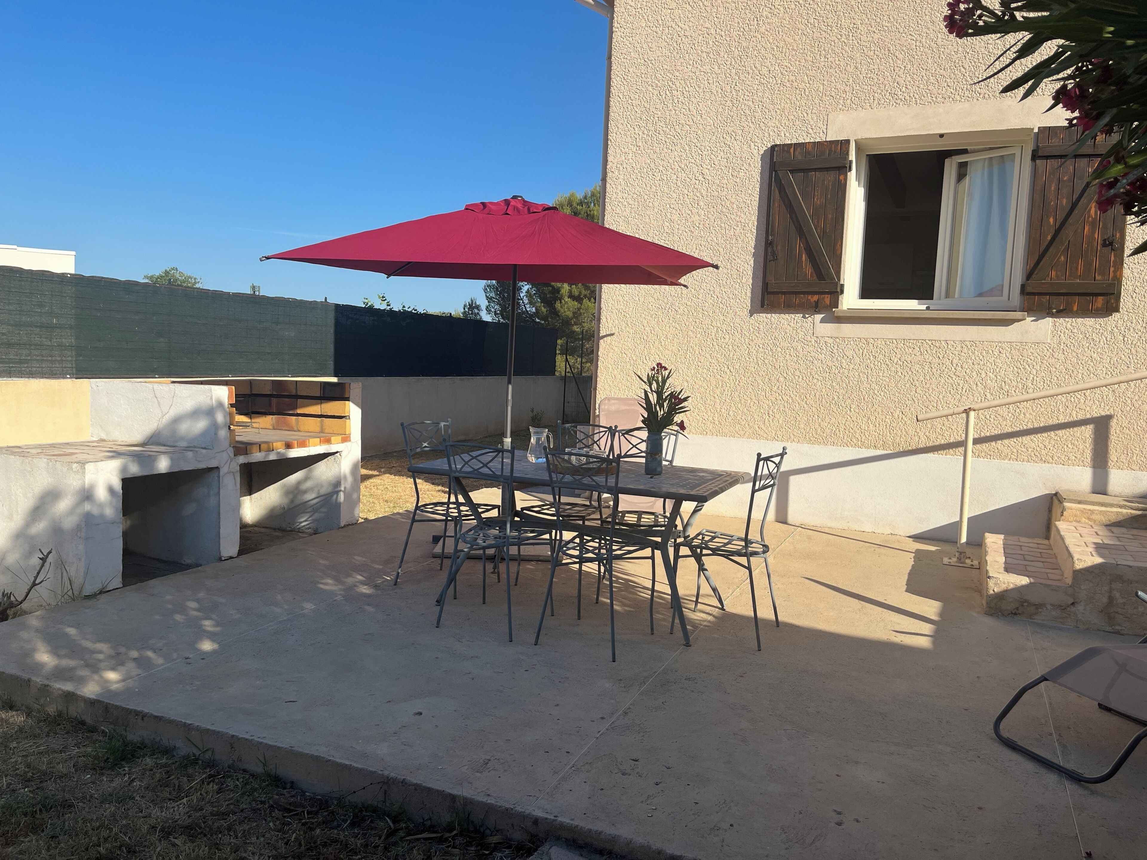An outdoor patio with a table and chairs, a red umbrella, and a small potted plant.