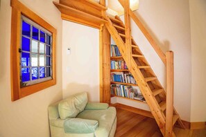 A room with a wooden staircase, a window with blue-tinted glass, and a bookshelf filled with books.
