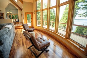 A room with a large window, a sofa, and two leather chairs.