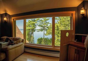 A room with a large window, a wooden bench, and a refrigerator.