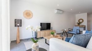 A modern living room with a sofa, coffee table, TV, and decorative items including orchids and a clock. - Galeão Sea Apartment - BY SCH (São Martinho do Porto)