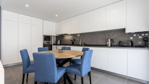 Eine moderne Küche mit weißen Schränken, einer schwarzen Arbeitsplatte und einem runden Holztisch mit blauen Stühlen.