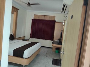 A bedroom with a bed, a desk, a wardrobe, a ceiling fan, and a door.