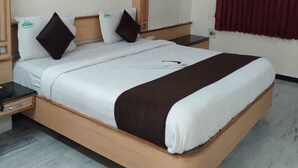 Une chambre d’hôtel avec un grand lit, une tête de lit en bois, un ventilateur de plafond, un rideau rouge et une armoire en bois.
