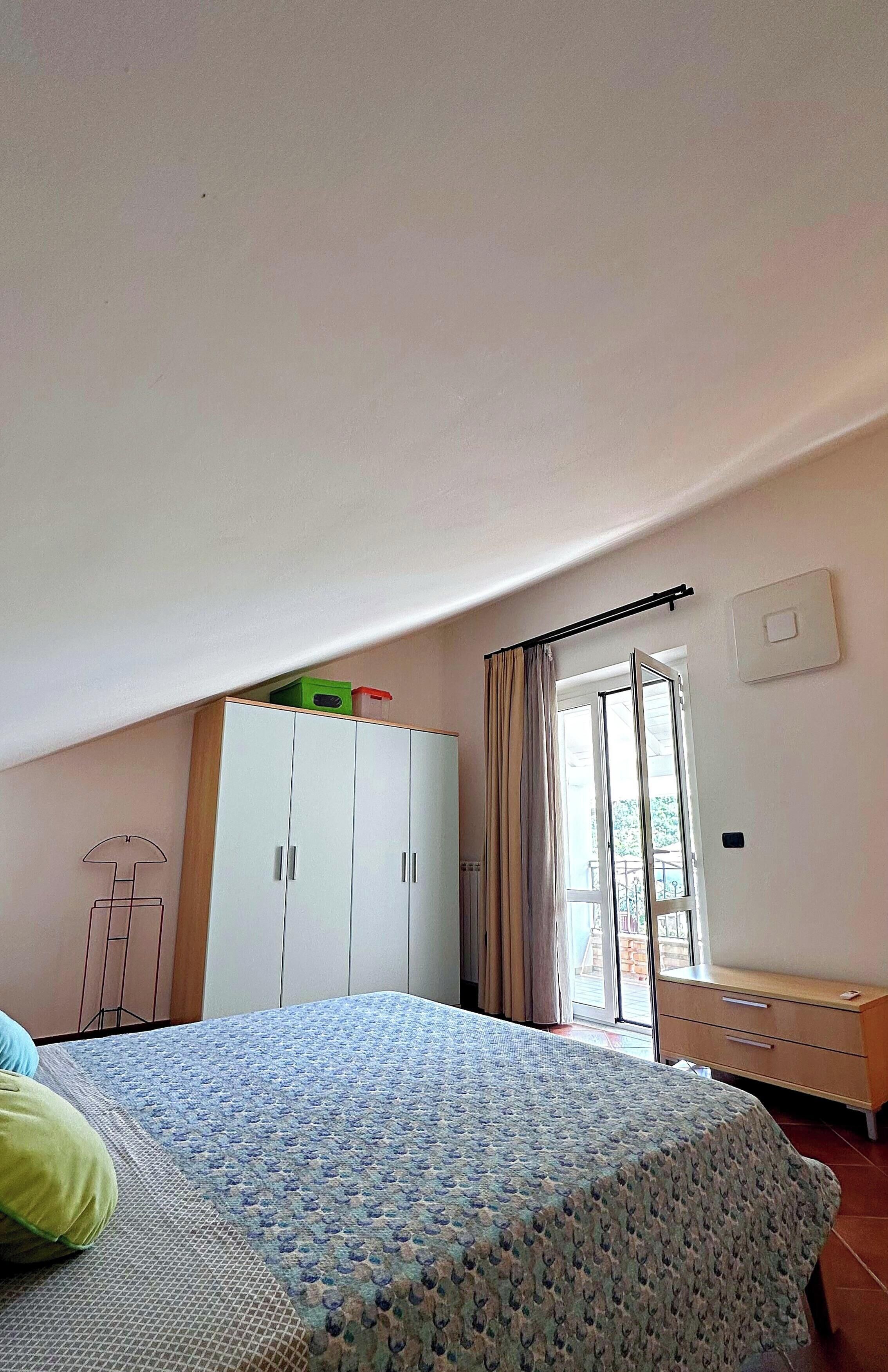 A bedroom with a bed, a wardrobe, a desk, and a window with curtains.
