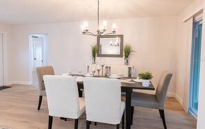 Ein Esszimmer mit einer Chandelüster, einem Spiegel und einer Zimmerpflanze.