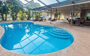 Ein Innenpool mit großen Glaswänden, umgeben von Liegestühlen und einer überdachten Sitzgruppe.